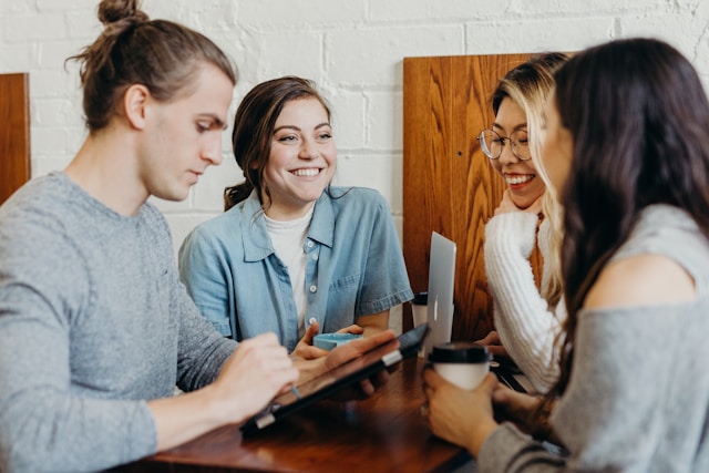 A group of friends at a brown table, smiling and reviewing text on a table screen.