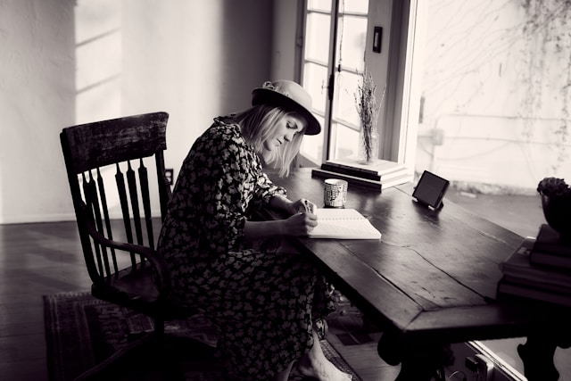Woman in floral dress sitting in chair writing in a notebook.