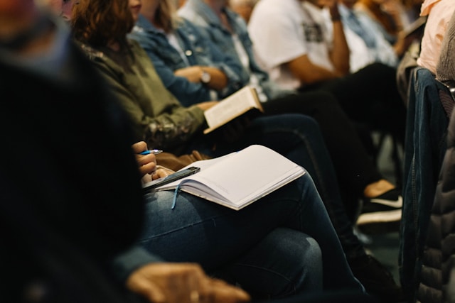 Closeup of a person writing in an open notebook in a conference room.