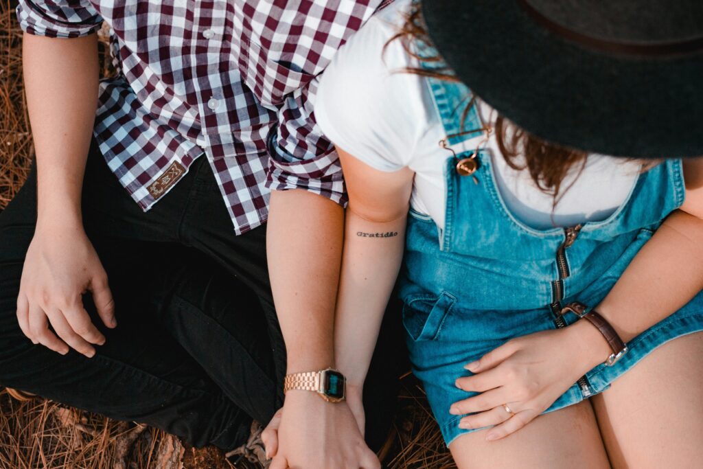 Humor and tension make your queer romance’s happy ending all the sweeter for your readers. Person in red-and-white checkered shirt and black pants holding hands with person in blue denim dress and white t-shirt.