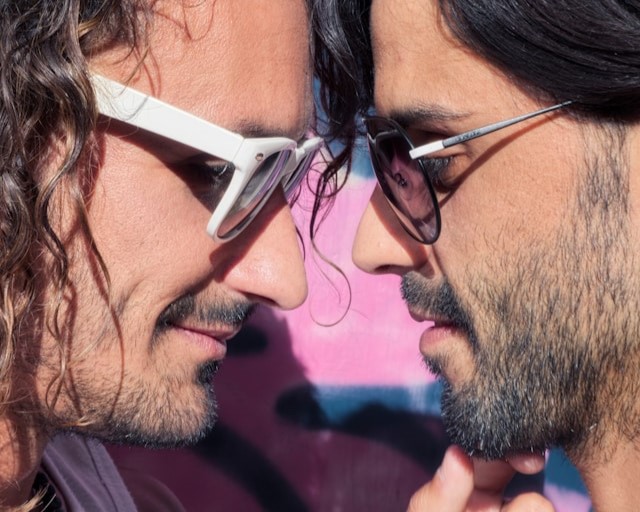 Emotional intimacy can be more powerful than the most explicit scenes in queer romance. Closeup of two men with foreheads pressed together, one cupping the other’s chin and grinning.